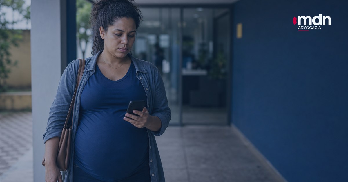 Imagem destacada - Fui mandada embora na experiência e estava grávida: o que fazer? Mulher grávida mandada embora na experiência olhando o celular na entrada do trabalho.